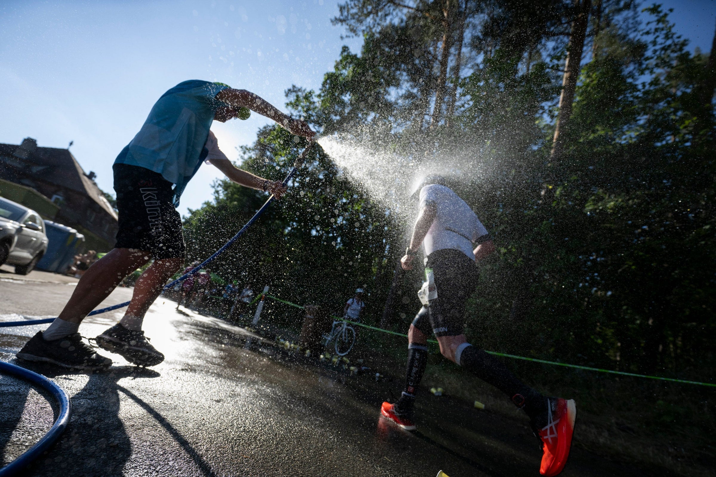 Beim DATEV Challenge Roth spritzt ein Helfer auf der Laufstrecke einen Athlethen mit Wasser ab um ihn abzukühlen